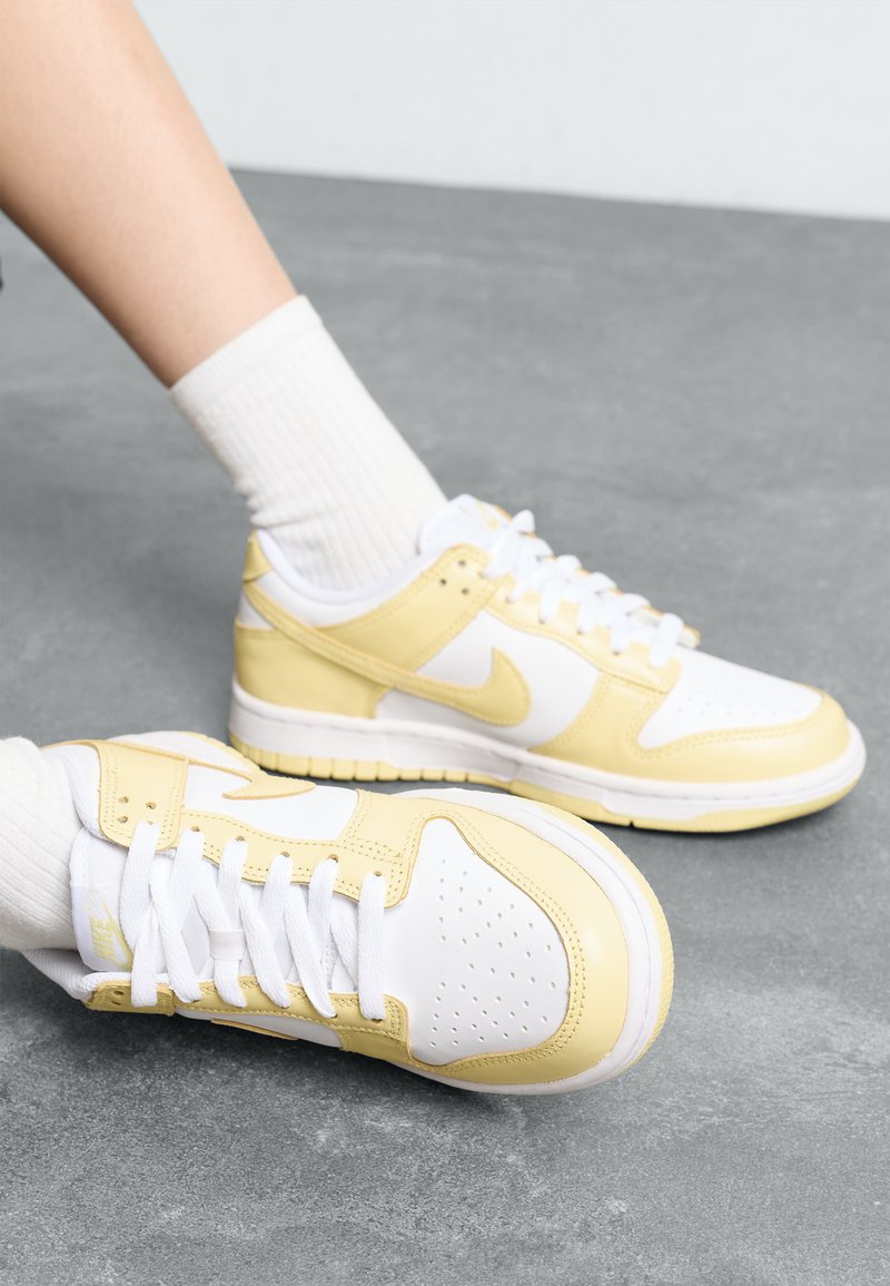 Sneakers Nike con una combinazione di colori bianco e giallo, realizzati in pelle e mesh, con punta perforata e design classico con lacci.