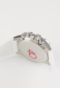 Witte chronograafhorloge met een zilveren roestvrijstalen kast, drie drukknoppen en een gestructureerde witte rubberen band. Bevat een rood logo op de achterkant.