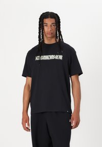 Čierne bavlnené tričko s kruhovým výstrihom, krátkymi rukávmi a veľkým zeleným nápisom "All Conditions Gear" na prednej strane. Voľný strih.