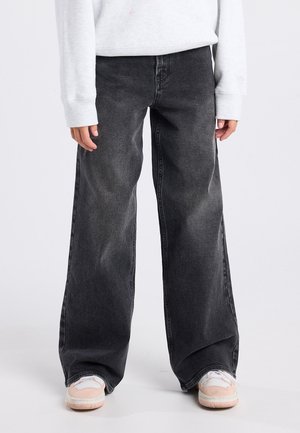 Jeans neri a gamba larga con una texture sbiadita, caratterizzati da una vita alta e un taglio dritto, abbinati a sneakers rosa chiaro.