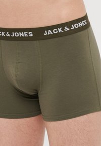 Boxers verts olive avec une texture douce et une ceinture élastique noire contrastante ornée du texte "JACK & JONES" en lettres blanches.