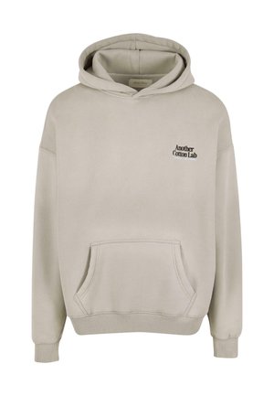Svetlo bež kapuca s puloverjem in sprednjim žepom ter majhnim črnim besedilom "Another Cotton Lab" na levem prsnem delu.