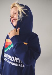 Navy blue hoodie featuring a large logo with red, green, and orange stripes. Made of soft fabric, includes a kangaroo pocket and drawstring hood.