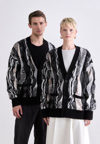 Knit cardigan with a geometric black and white pattern, ribbed cuffs and hem, featuring buttons and front pockets.