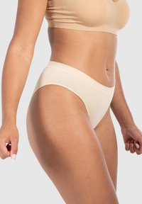 Mutande beige a coste con un ampio elastico in vita, dotate di un design senza cuciture e una superficie liscia, posizionate su uno sfondo neutro.