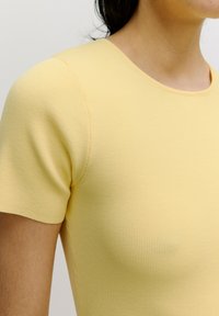Gelbes geripptes Shirt mit kurzen Ärmeln und Rundhalsausschnitt. Verfügt über sichtbare Nahtdetails, einen weichen Stoff und eine figurbetonte Passform.