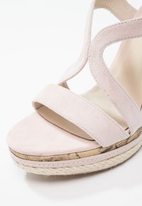 Sandale compensée en daim rose clair avec deux brides, bordure en liège et semelle plate-forme enveloppée de corde sur fond blanc.