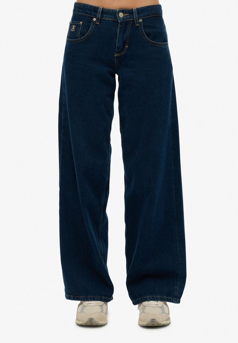Jeans de tiro ancho de color azul oscuro, fabricados en denim. Presentan bolsillos frontales, un cierre de botón y detalles de costura a lo largo de las costuras.