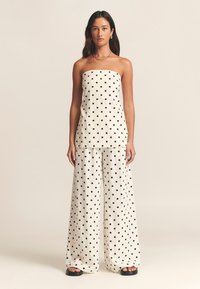 White strapless top with black polka dots, paired with wide-leg pants of the same design. Smooth texture, casual fit, and no visible hardware.
