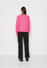 Fuchsia tröja med texturerad yta, kort längd och långa ärmar, i kombination med svarta cargobyxor och kraftiga svarta skor.