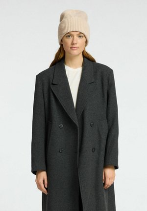 Grijs wollen dubbelzijdig jasje met geknipte revers, gecombineerd met een beige gebreide beanie. Het heeft grote knopen en lange mouwen.