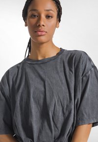 Donkergrijs katoenen T-shirt met een losse pasvorm, ronde hals en korte mouwen. Heeft een zachte, gestructureerde oppervlakte met zichtbare kreukels.