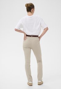 T-shirt blanche surdimensionnée, pantalons ajustés beiges, ceinture marron et chaussures claires. Tissu lisse, peu de détails et coupe décontractée.