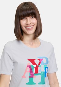Lichtgrijs T-shirt met korte mouwen, voorzien van een kleurrijke grafiek van stapelende letters in roze, rood, groen en blauw met glanzende accenten.