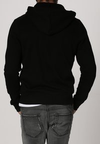 Zwarte katoenen hoodie met een trekkoordcapuchon, ribgebreide manchetten en zoom. Gemaakt met grijze denim jeans met versleten details op de zakken.