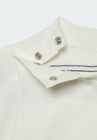 Collo di polo bianco in cotone con bottoni a pressione argentati e dettagli a strisce nere. Tessuto morbido con un design del colletto strutturato.