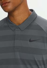 Polo shirt Nike grigio scuro con strisce nere, dotato di un colletto e tessuto testurizzato. Logo esposto sul lato sinistro del petto.