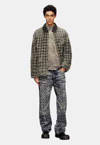 Veste matelassée pour homme en motif pied de poule, grise et noire, associée à un pull gris texturé et à un jean bleu motif, avec des chaussures noires.