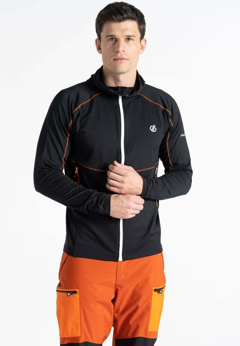 Schwarze Jacke mit orangefarbenen Akzenten und durchgehendem Reißverschluss, kombiniert mit orangen Hosen mit seitlichen Taschen. Gleiche Materialstruktur und athletischer Schnitt.