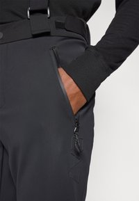 Μαύρο τεχνικό παντελόνι με ομαλή υφή, τσέπη με φερμουάρ και γυαλιστερή επένδυση, καθώς και με λογότυπο της μάρκας χαραγμένο στο ύφασμα.