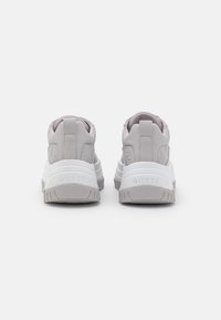 Et par lysegrå Guess-sneakers vist fra bagsiden, med tykke hvide såler og prægede brandnavn på hælen.