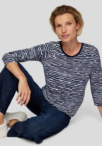 Navy und weißes Langarmshirt mit horizontalem Streifenmuster. Hat einen runden Ausschnitt und eine lockere Passform, kombiniert mit dunklen Jeans und Sneakern.