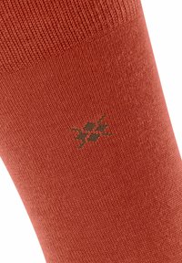 Calza in cotone di colore arancione ruggine, con un motivo di maglia texturizzato. Un piccolo logo di colore verde scuro è posizionato sulla parte superiore.