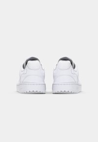 Zapatillas blancas con parte superior de cuero suave, cuello acolchado y suela de goma texturizada. Detalles de costura sutil y diseño minimalista.