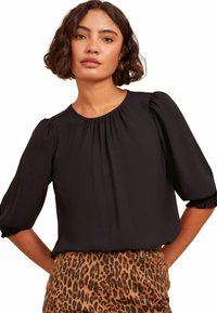 Blusa nera con maniche a sbuffo e scollatura arricciata, abbinata a pantaloni a fantasia leopardo marroni con tasche. Tessuto dal tocco morbido.