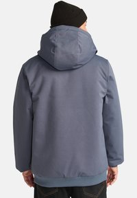 Blå huva jacka med en mjuk textur och elastiska ärmslut. Har en ribbad nederkant och en tättslutande huva. Enkel, funktionell design.