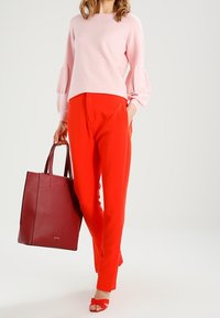 Lichtroze trui met pofmouwen, rode op maat gemaakte broek, rode hoge hakken, en een gestructureerde rode tote bag. Glamoureuze texturen en heldere kleuren.