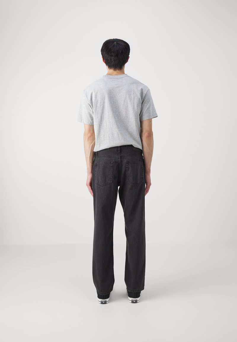 Graues T-Shirt mit kurzen Ärmeln, kombiniert mit schwarzen geraden Jeans. Der Stoff scheint aus Baumwolle zu sein, mit sichtbaren Nähten und Taschen an den Jeans.