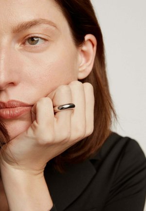 Anillo de banda ancha de plata llevado en un dedo, superficie lisa con un acabado pulido, contra un fondo suavemente iluminado con tonos neutros.