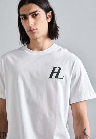 Valge puuvillane T-särk, millel on must "HL" logo vasakul rinnal. Lühikesed varrukad ja klassikaline ümmargune kaelus. Sile tekstuur.