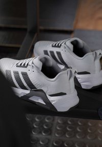 Ζευγάρι λευκά και μαύρα αθλητικά παπούτσια Adidas τοποθετημένα σε ένα σκοτεινό παγκάκι με θολό φόντο.