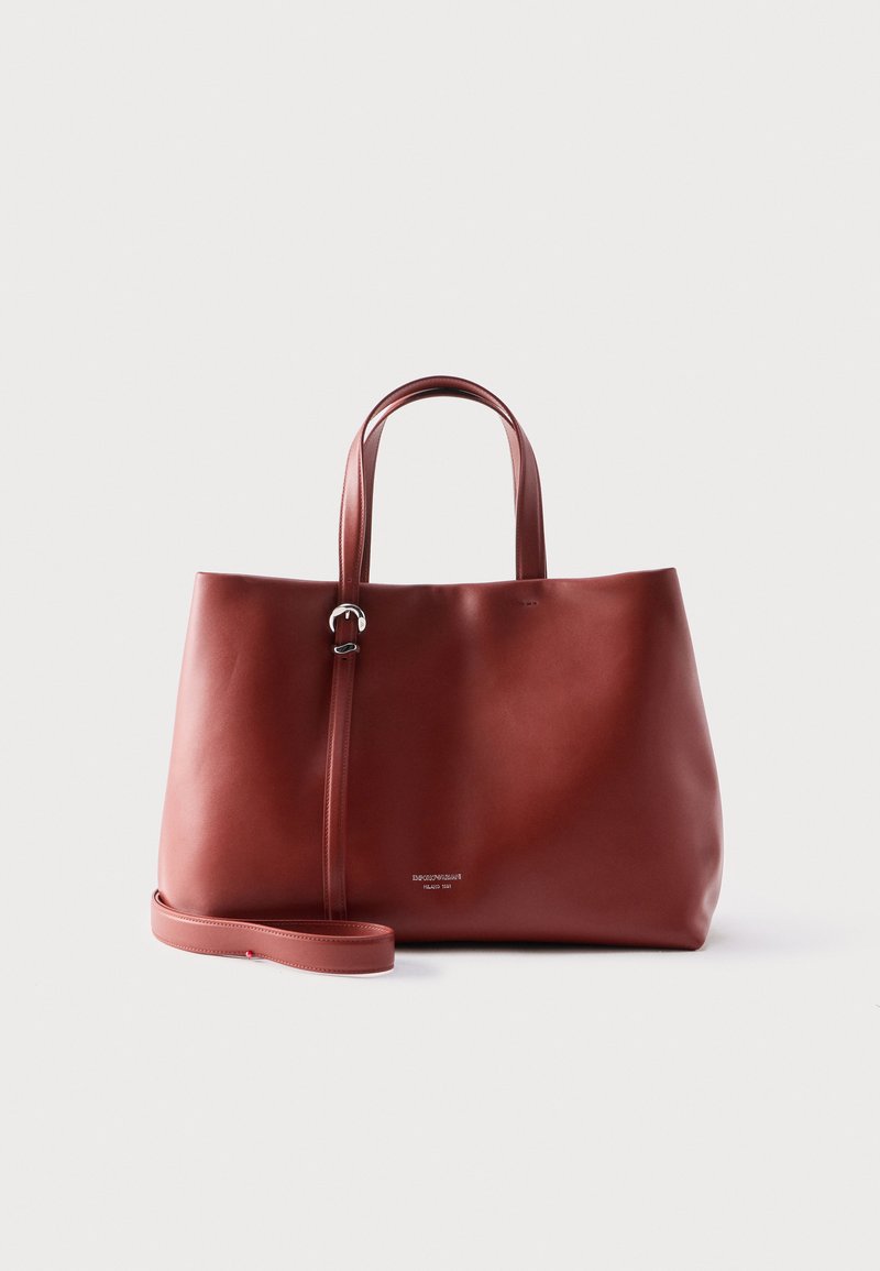 Sac fourre-tout en cuir marron avec double poignée et bandoulière réglable, présenté sur un fond clair uni.