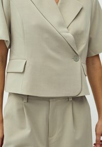 Lichtgrijze op maat gemaakte blazer met een gelapte kraag, korte mouwen en een enkele knoopsluiting, gecombineerd met bijpassende broeken.