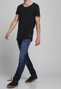 Camiseta negra de manga corta con escote redondo, combinada con jeans de mezclilla azul y zapatillas negras con suela de goma marrón.