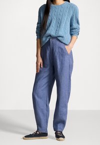 Světlomodrý svetr s copánkovým vzorem ve spojení s volně střiženými světle modrými lněnými kalhotami a černými espadrilkami s béžovými akcenty.