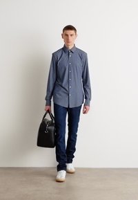 Camicia a righe blu navy, jeans scuri, sneakers bianche e una borsa in pelle nera. La camicia è dotata di colletto e maniche lunghe.