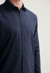 Marineblauwe langetermijns-overhemd gemaakt van textuurstof, met een button-down kraag en een klein logo op de borst. Vijf knopen zichtbaar.