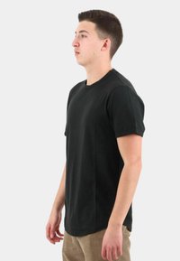 T-shirt nero a maniche corte realizzato in un tessuto morbido. Presenta un collo a giro e una vestibilità comoda, mostrato su una persona di profilo.