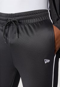 Black athletic joggers with an elastic waistband, drawstring detail, side white stripes, and a small embroidered logo on the thigh.