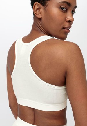 Reggiseno sportivo bianco a coste con design racerback, caratterizzato da un ampio elastico e una texture morbida, che mette in risalto una silhouette aderente.