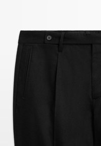 Svarta skräddarsydda byxor med en slät yta, med knäppning, bälteshällor och sidofickor. Klassisk design med en formell estetik.
