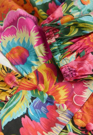 Tissu floral avec des motifs vifs de rose, jaune et bleu, au toucher texturé et tissé, avec une bordure élastique.