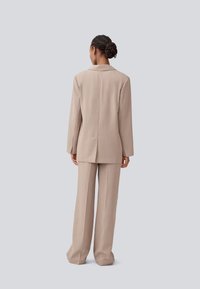 Beige tailored suit with a single-breasted blazer, long sleeves, and wide-leg trousers, featuring a smooth texture and structured design.