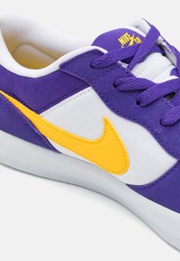 Baskets violettes et blanches avec un swoosh jaune, dotées d'une tige en toile, d'accents en daim texturé et d'une semelle en caoutchouc.