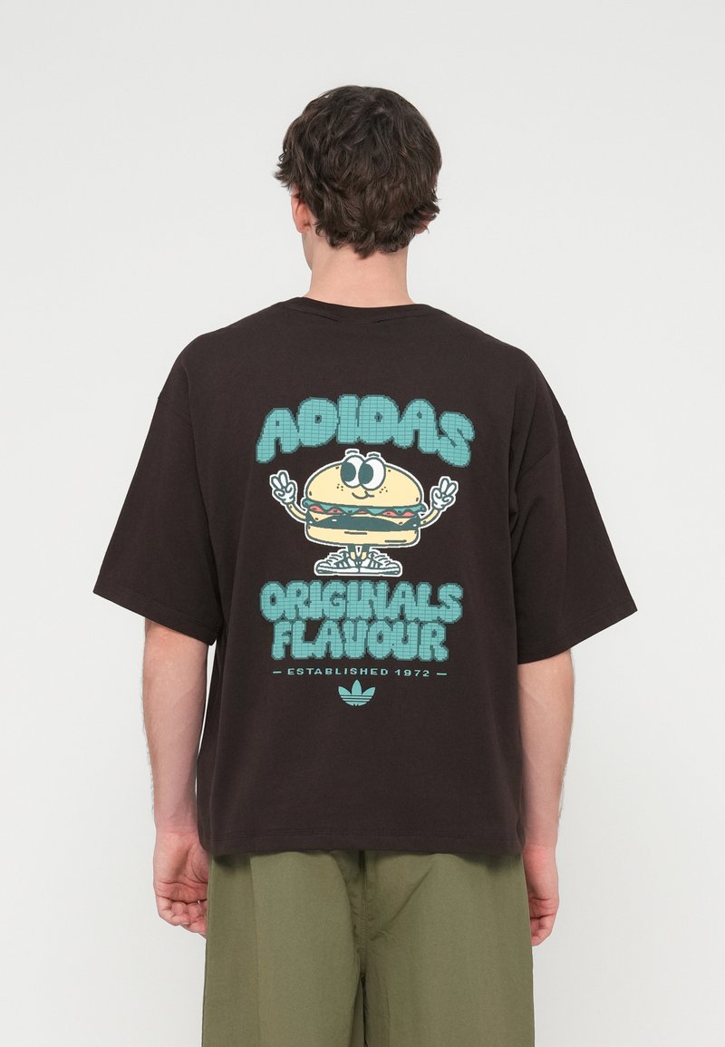 Μαύρο υπερμεγέθες T-shirt με πολύχρωμο γραφικό ενός μπέργκερ με χαμογελαστό πρόσωπο, συνοδευόμενο από το κείμενο "ADIDAS ORIGINALS FLAVOUR" από κάτω.