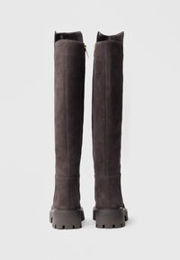 Długie, ciemnoszare zamszowe buty z płaską, grubą podeszwą. Posiadają zamek błyskawiczny z tyłu oraz usztywnione górne krawędzie. Gładka faktura.